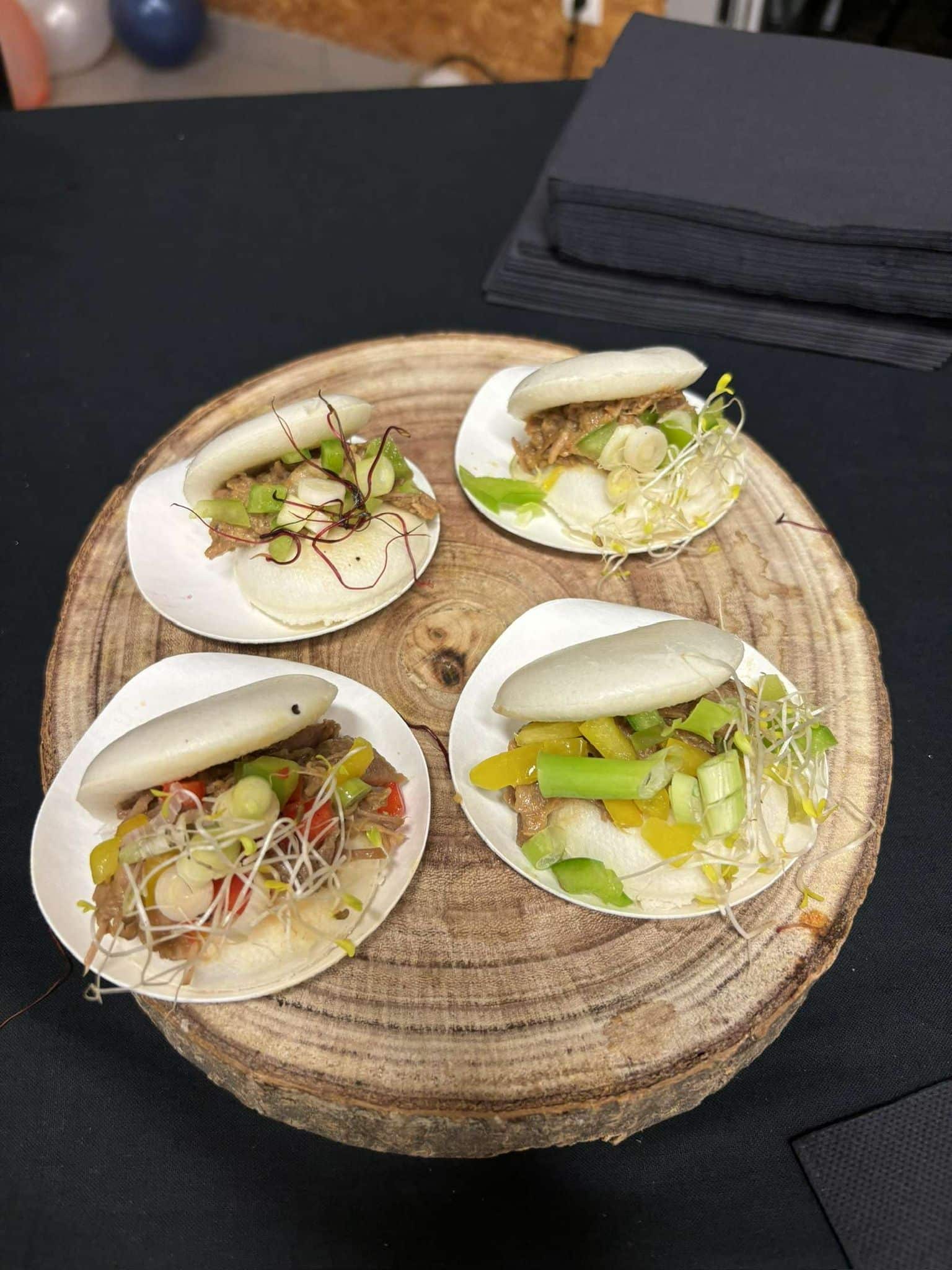 Quatre sandwichs bao aux légumes et viande présentés sur une tranche de bois
