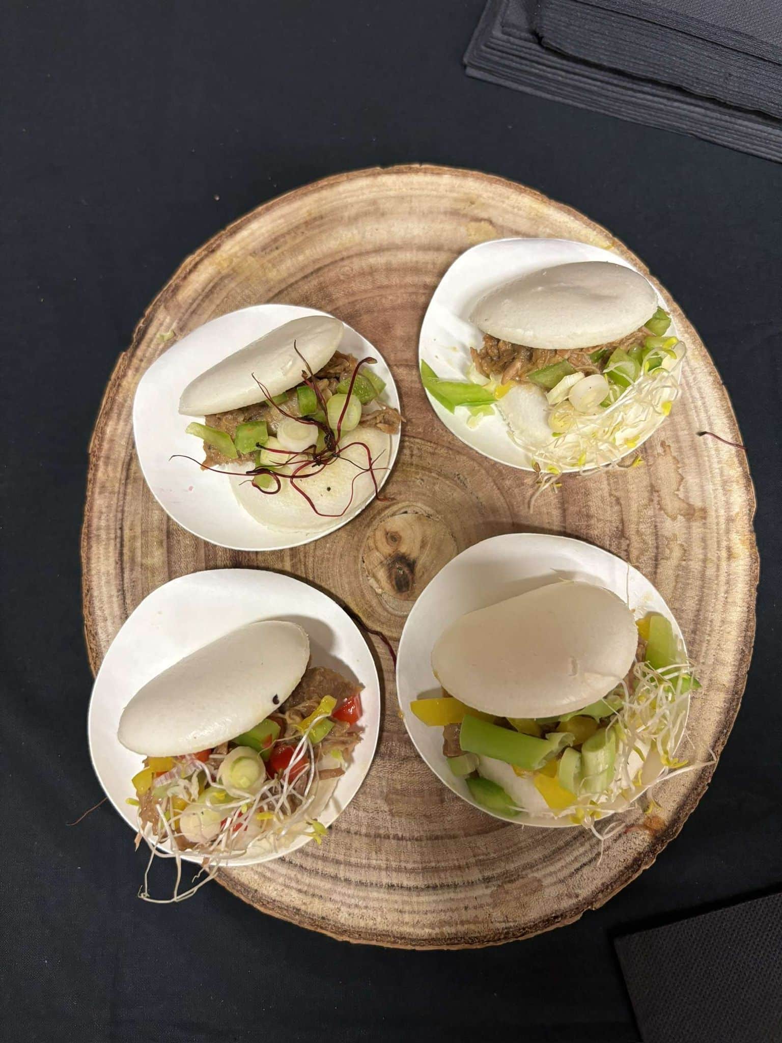 Quatre petits sandwichs vapeurs garnis de viande et légumes sur une planche en bois
