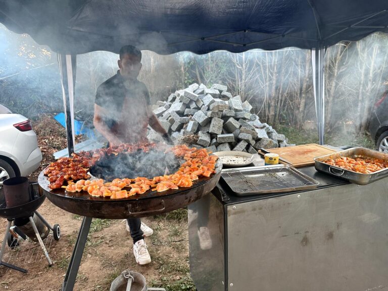 Homme cuisant des brochettes sur un gril circulaire fumant en extérieur sous un barnum
